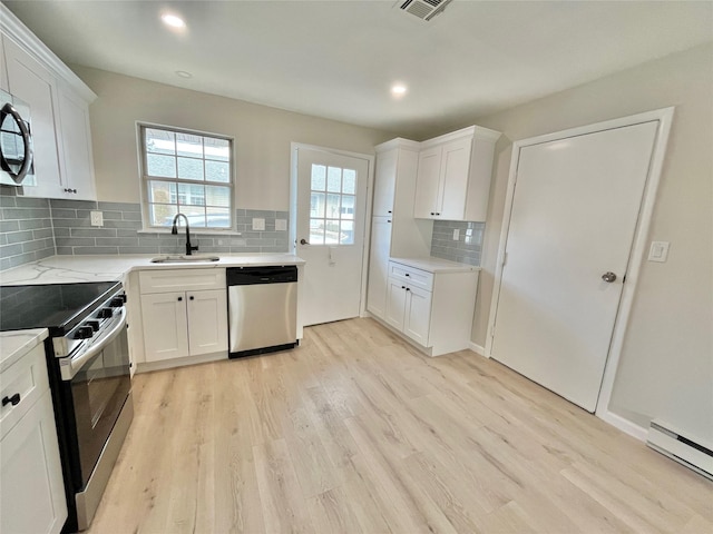 kitchen featuring light wood finished floors, baseboard heating, stainless steel appliances, white cabinetry, and a sink