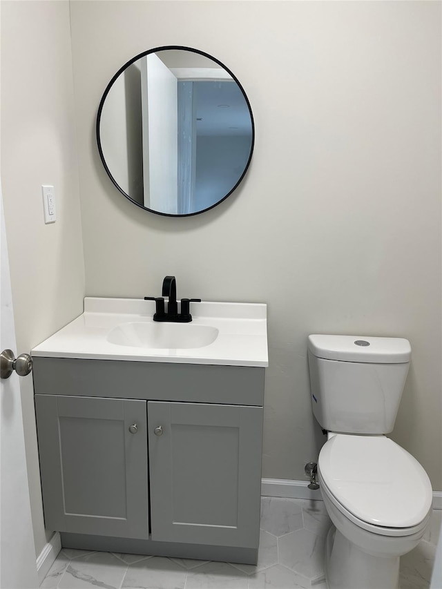 half bathroom with toilet, marble finish floor, vanity, and baseboards