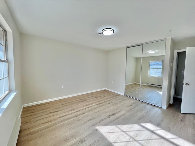 unfurnished bedroom featuring a baseboard heating unit, visible vents, baseboards, light wood-style floors, and a closet