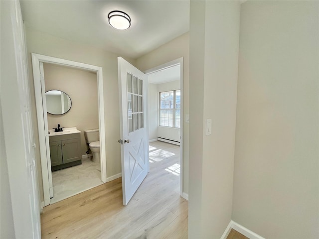 hall with light wood-type flooring, baseboards, a sink, and baseboard heating