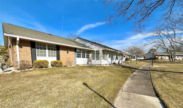 ranch-style home with a sunroom, a shingled roof, a front lawn, and brick siding