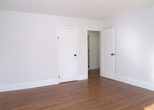 unfurnished room with baseboards and dark wood-type flooring