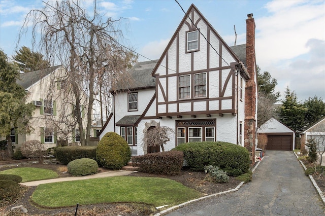 english style home with an outbuilding, a detached garage, roof with shingles, stucco siding, and a chimney