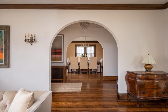 hallway with a chandelier, arched walkways, baseboards, ornamental molding, and dark wood finished floors