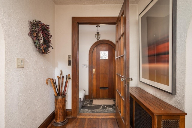 doorway to outside with dark wood-style floors, a textured wall, arched walkways, and baseboards