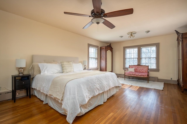 bedroom with a baseboard radiator, wood finished floors, a ceiling fan, and baseboards