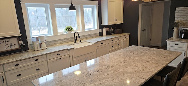 kitchen with white cabinetry, a sink, light stone countertops, and pendant lighting