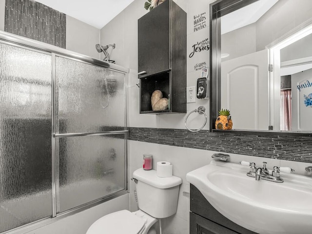 full bath featuring decorative backsplash, toilet, combined bath / shower with glass door, vanity, and tile walls