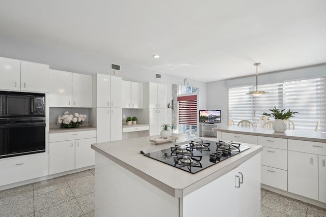 kitchen with white cabinets, a kitchen island, black appliances, granite finish floor, and pendant lighting