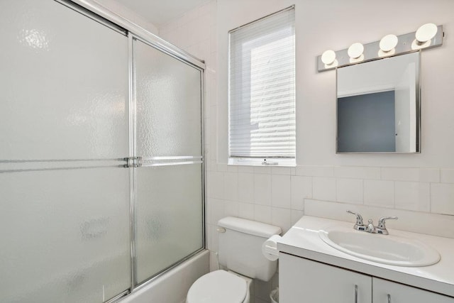 full bath featuring toilet, bath / shower combo with glass door, tile walls, and vanity