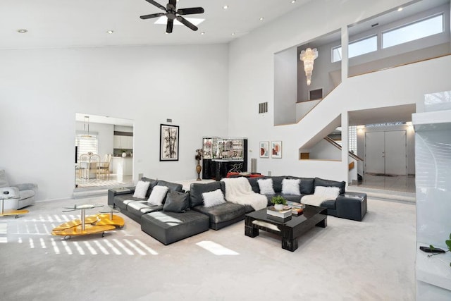 carpeted living area with visible vents, stairway, a towering ceiling, and a ceiling fan