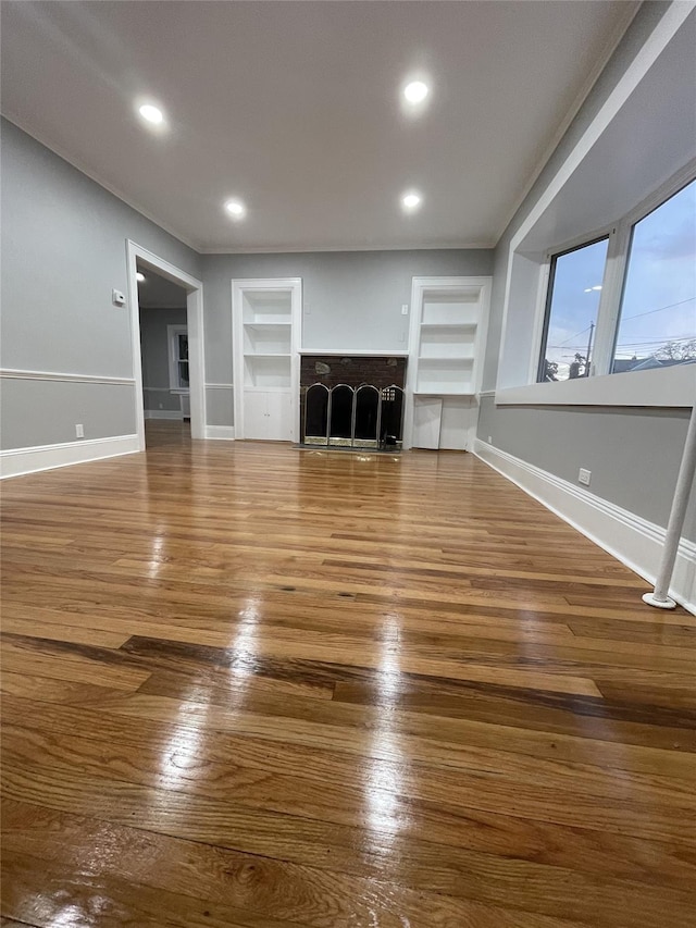 unfurnished living room with built in shelves, a fireplace, recessed lighting, wood finished floors, and baseboards