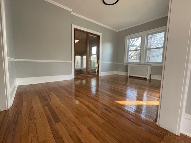 spare room with radiator, baseboards, crown molding, and wood finished floors