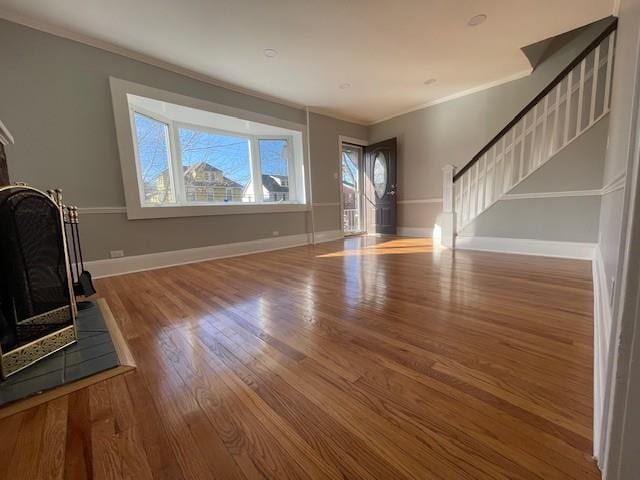 unfurnished living room with stairs, crown molding, wood finished floors, and baseboards