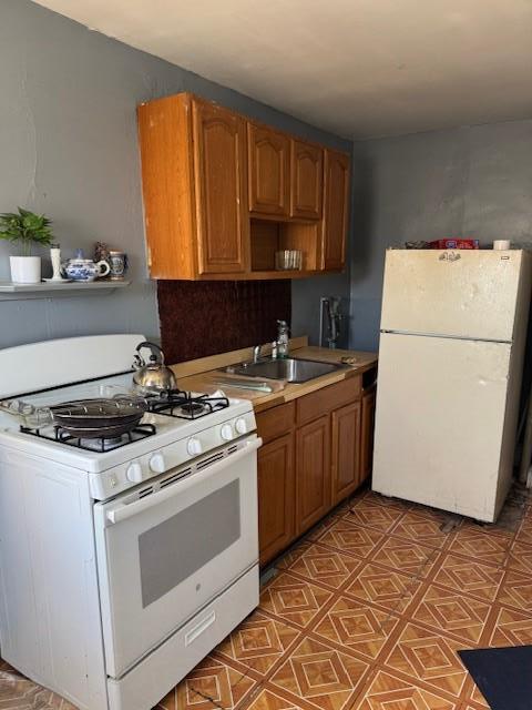 kitchen with brown cabinets, open shelves, light countertops, a sink, and white appliances