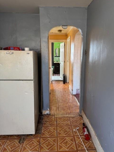 corridor featuring arched walkways, baseboards, and tile patterned floors