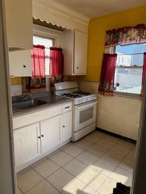 kitchen featuring light tile patterned floors, brick wall, a sink, white cabinets, and gas range gas stove