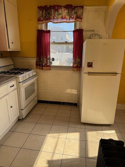 kitchen with white appliances, light tile patterned flooring, and white cabinetry