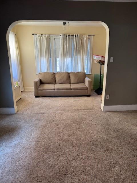 unfurnished living room with arched walkways, light carpet, and baseboards