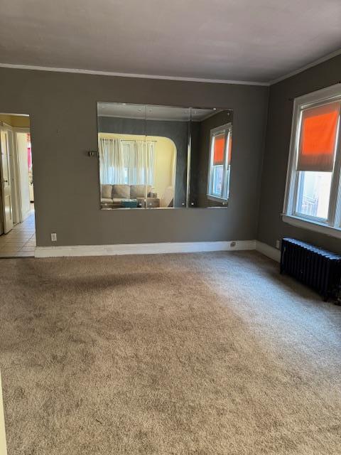 empty room featuring baseboards, light colored carpet, crown molding, and radiator heating unit