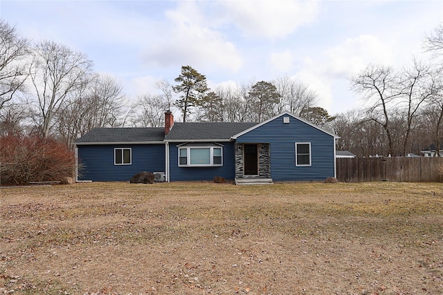 ranch-style home with a shingled roof, a chimney, fence, and a front lawn