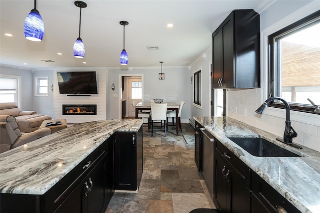 kitchen with stone tile flooring, ornamental molding, a sink, and decorative light fixtures