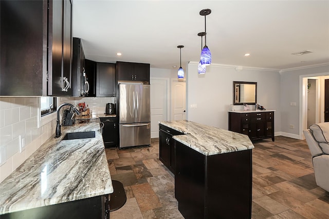 kitchen with a sink, a kitchen island, freestanding refrigerator, light stone countertops, and decorative light fixtures