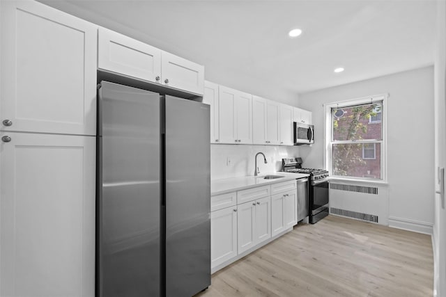 kitchen with a sink, white cabinets, light countertops, appliances with stainless steel finishes, and radiator