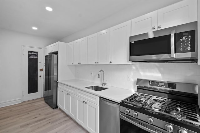 kitchen featuring white cabinets, stainless steel appliances, light countertops, light wood-type flooring, and a sink