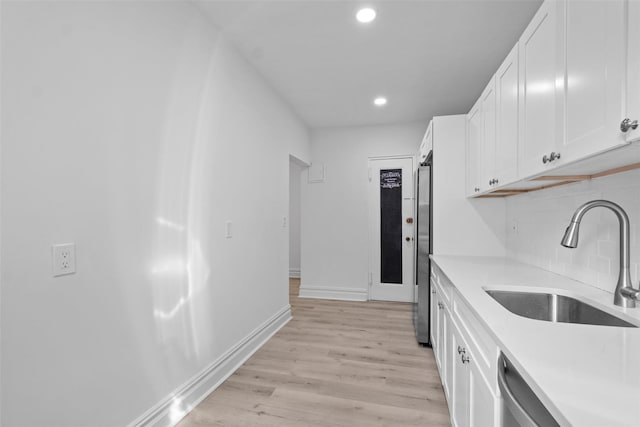 kitchen with a sink, white cabinets, light countertops, light wood-type flooring, and decorative backsplash