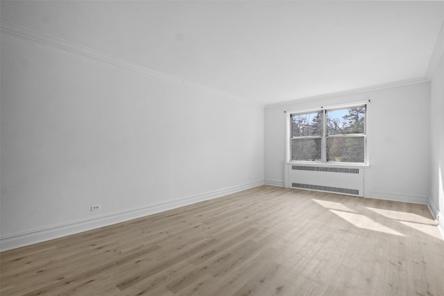 spare room with baseboards, ornamental molding, light wood-type flooring, and radiator