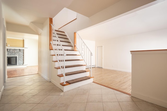 staircase with a brick fireplace, a baseboard radiator, baseboards, and tile patterned floors