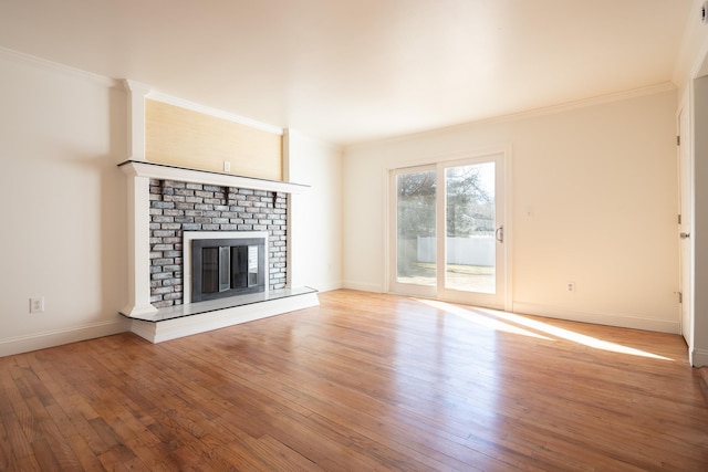 unfurnished living room featuring a brick fireplace, crown molding, baseboards, and wood finished floors