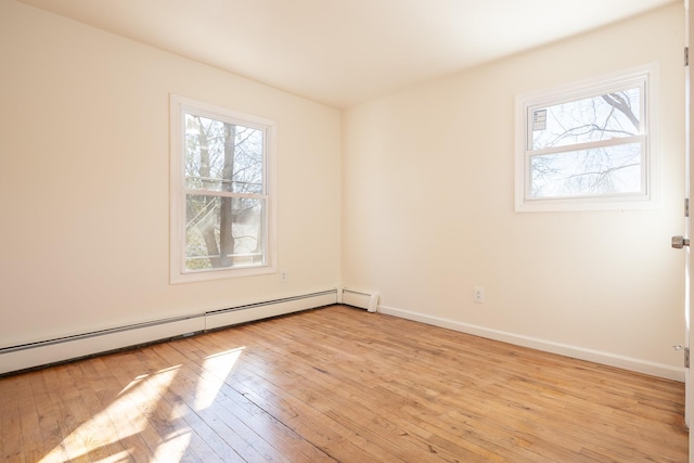 unfurnished room featuring light wood finished floors, baseboard heating, a wealth of natural light, and baseboards