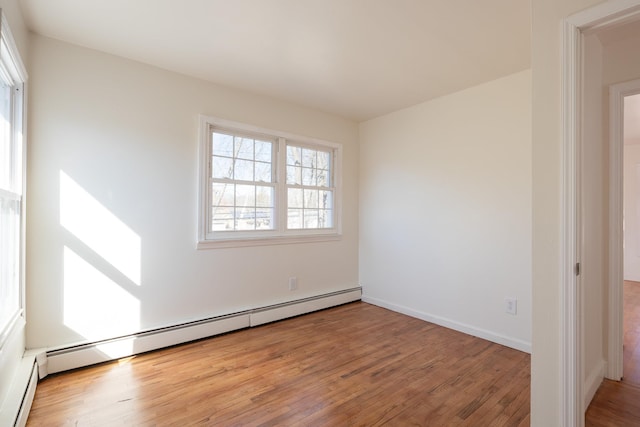 empty room with a baseboard heating unit, baseboards, and light wood finished floors