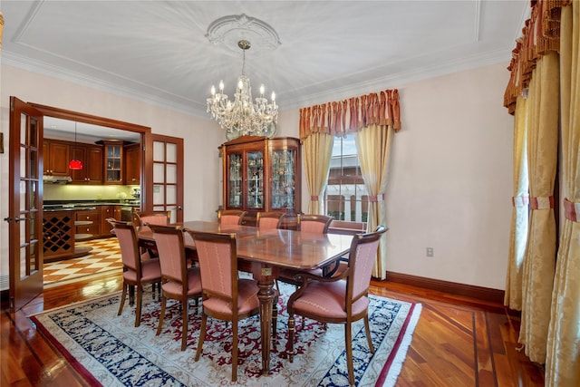 dining area featuring a chandelier, ornamental molding, baseboards, and wood finished floors