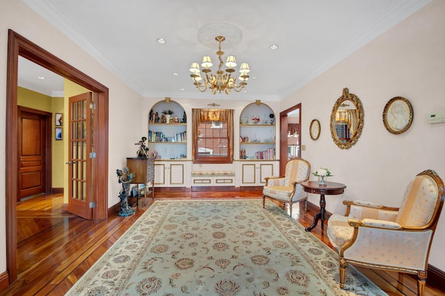 sitting room featuring hardwood / wood-style flooring, a notable chandelier, baseboards, built in features, and crown molding