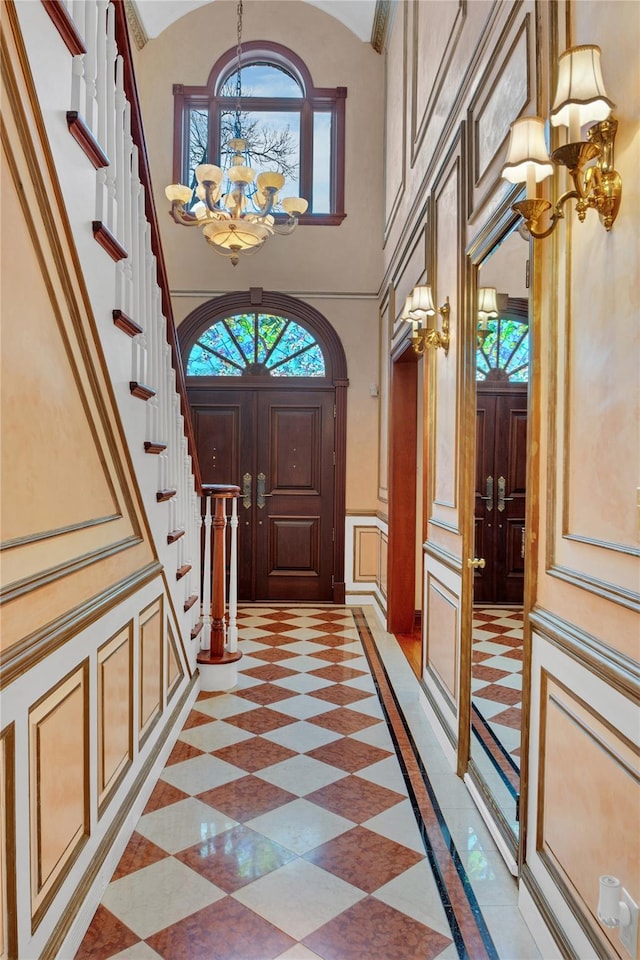 entrance foyer featuring vaulted ceiling, a notable chandelier, a decorative wall, and stairs