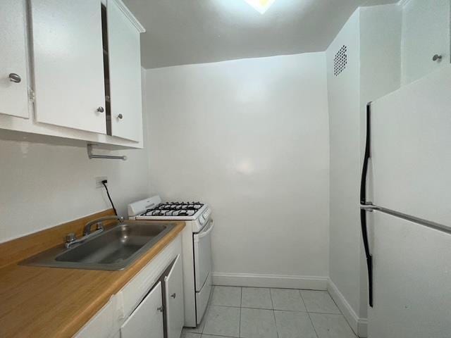 kitchen featuring a sink, white appliances, light tile patterned floors, and white cabinetry