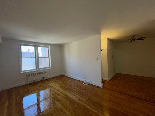 unfurnished room featuring radiator heating unit, wood finished floors, baseboards, and ceiling fan