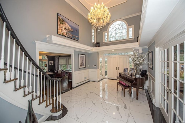 entrance foyer with wainscoting, ornamental molding, marble finish floor, stairs, and a chandelier