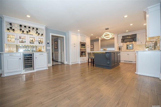 interior space featuring wine cooler, a breakfast bar area, decorative light fixtures, light countertops, and white cabinetry