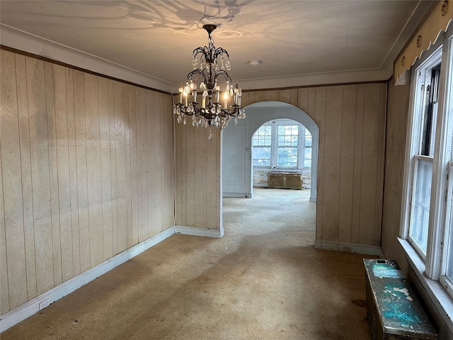 unfurnished dining area with light carpet, wooden walls, arched walkways, and crown molding