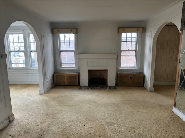 unfurnished living room with arched walkways, a brick fireplace, and light carpet