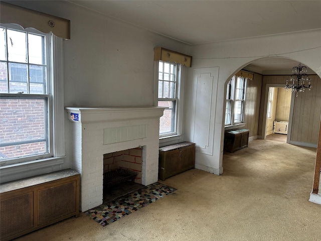 unfurnished living room featuring arched walkways, a chandelier, light carpet, a fireplace, and radiator