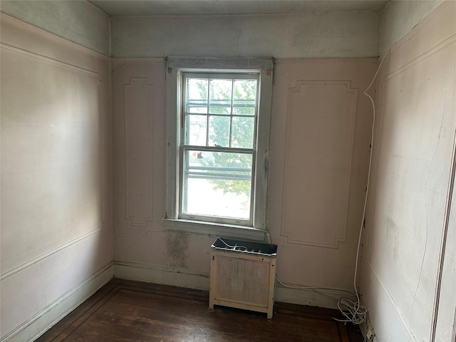 empty room featuring dark wood-style floors, plenty of natural light, and radiator heating unit