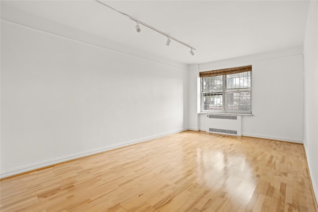 empty room featuring light wood finished floors, radiator heating unit, rail lighting, and baseboards