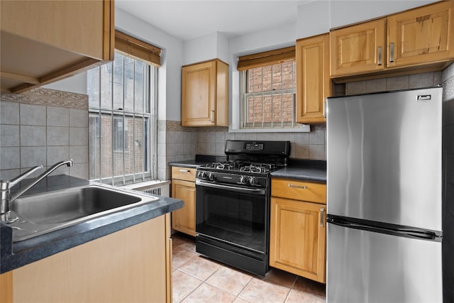 kitchen with light tile patterned floors, dark countertops, black gas range oven, freestanding refrigerator, and a sink