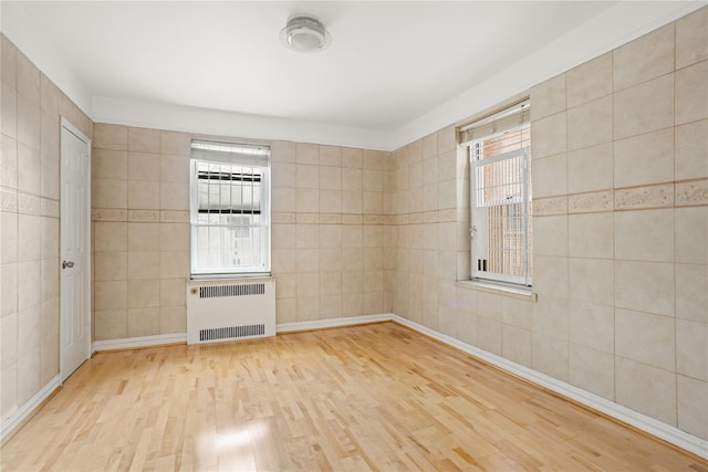 empty room with tile walls, radiator heating unit, and light wood finished floors