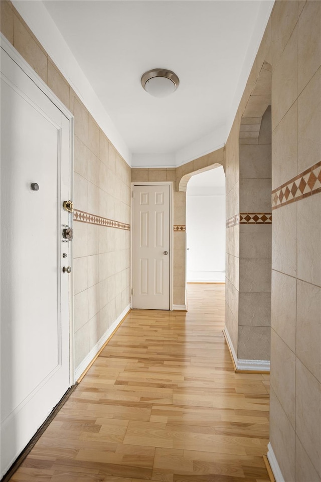 corridor featuring arched walkways, tile walls, and wood finished floors